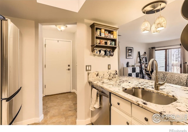 kitchen with a sink, white cabinets, appliances with stainless steel finishes, light stone countertops, and decorative light fixtures