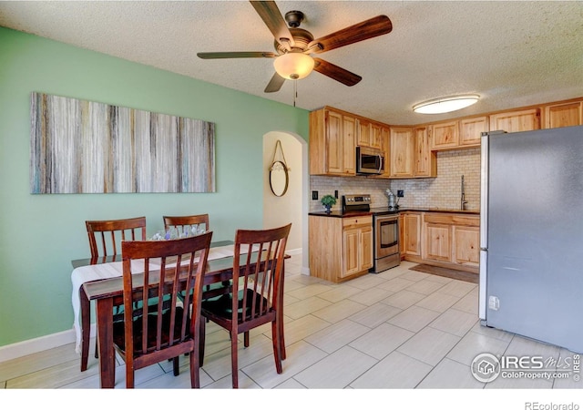 kitchen with dark countertops, appliances with stainless steel finishes, backsplash, light brown cabinetry, and a sink