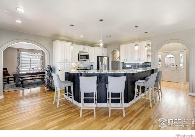 kitchen with arched walkways, light wood finished floors, appliances with stainless steel finishes, white cabinetry, and a kitchen bar