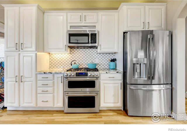 kitchen with appliances with stainless steel finishes, backsplash, light stone countertops, and white cabinets