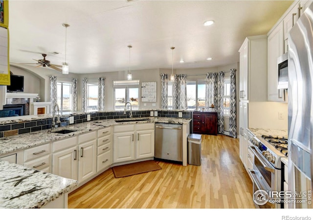 kitchen with appliances with stainless steel finishes, white cabinets, a sink, and light wood-style flooring