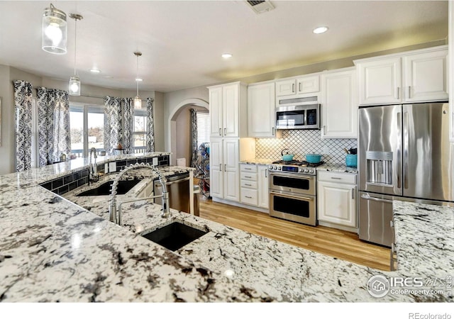 kitchen with appliances with stainless steel finishes, arched walkways, white cabinets, and light stone countertops