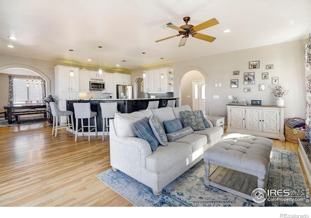 living room featuring light wood-style floors, arched walkways, visible vents, and recessed lighting