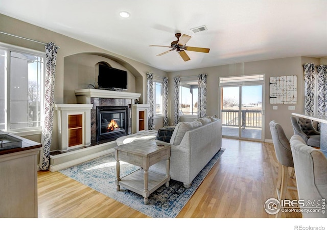 living area featuring a ceiling fan, a high end fireplace, visible vents, and wood finished floors