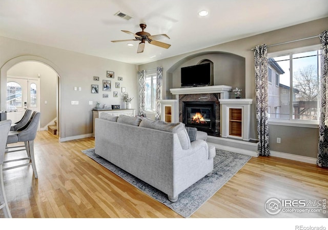 living area with a wealth of natural light, arched walkways, visible vents, and light wood-style floors