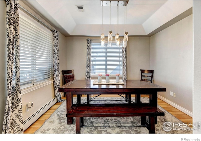 dining space with a baseboard radiator, visible vents, light wood finished floors, and a tray ceiling