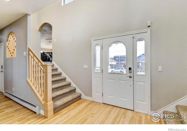 entryway with baseboards, arched walkways, a baseboard radiator, stairway, and wood finished floors