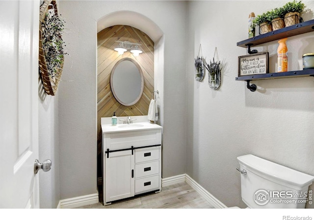 bathroom with toilet, baseboards, wood finished floors, and vanity