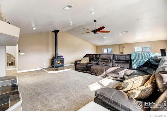 living room featuring carpet, a wood stove, visible vents, and vaulted ceiling