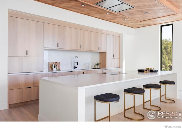 kitchen with wooden ceiling, light wood-style flooring, a breakfast bar area, light countertops, and backsplash