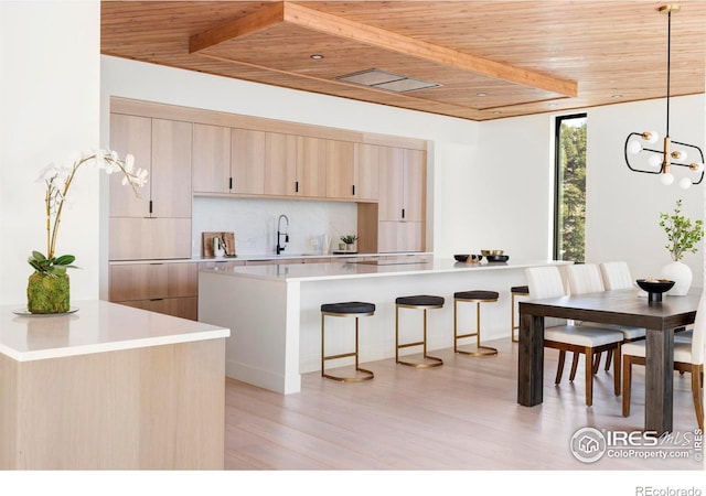 kitchen with a breakfast bar area, tasteful backsplash, light countertops, light brown cabinetry, and wood ceiling