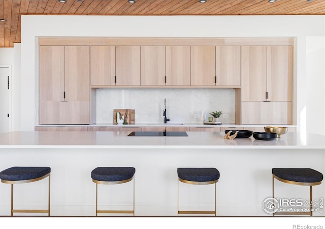 kitchen with a breakfast bar, a sink, backsplash, and light brown cabinetry