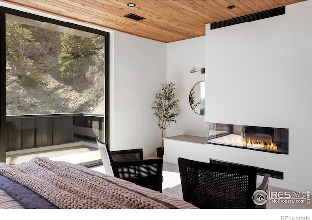 bedroom with a wall of windows, wooden ceiling, and a glass covered fireplace