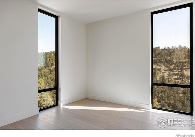 empty room with expansive windows, wood-type flooring, and baseboards