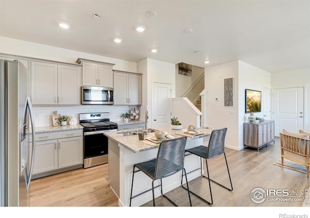 kitchen with gray cabinetry, stainless steel appliances, a sink, a kitchen breakfast bar, and decorative backsplash