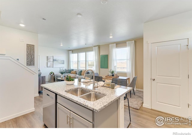 kitchen featuring light wood-style flooring, a kitchen island with sink, a sink, open floor plan, and stainless steel dishwasher