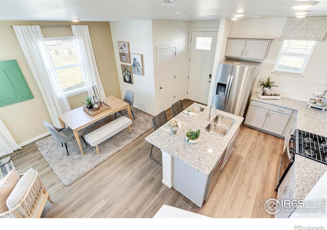 kitchen with a sink, stainless steel refrigerator with ice dispenser, a center island with sink, and light wood finished floors