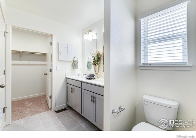 bathroom featuring double vanity, baseboards, toilet, tile patterned flooring, and a spacious closet