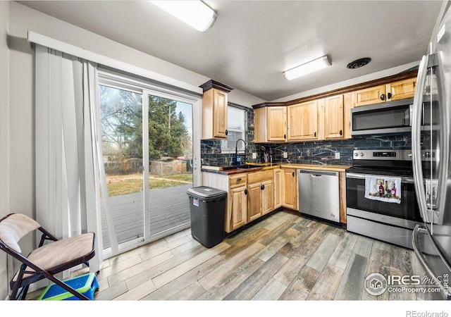 kitchen with tasteful backsplash, dark countertops, light wood-style flooring, appliances with stainless steel finishes, and a sink