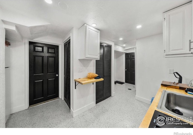 kitchen with recessed lighting, wooden counters, white cabinetry, a sink, and baseboards