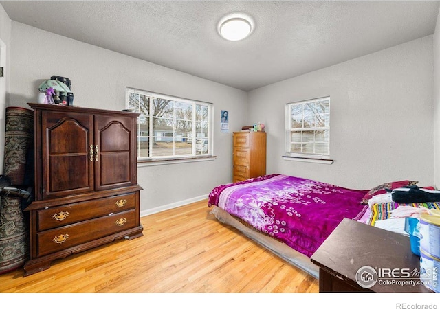 bedroom featuring light wood-style floors, baseboards, and a textured ceiling