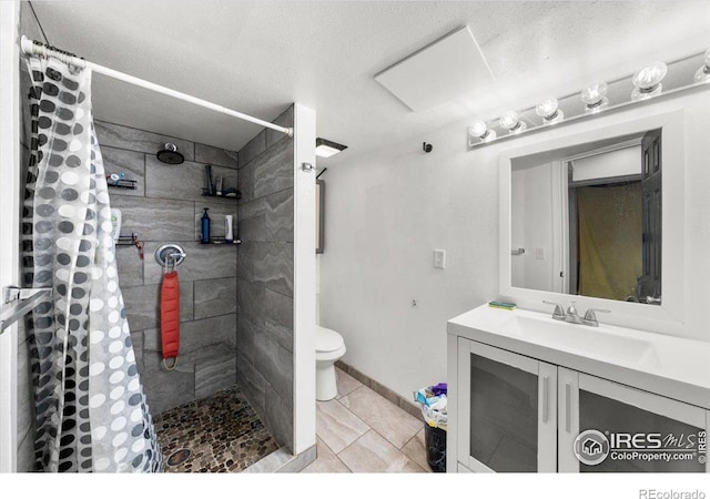 full bathroom featuring toilet, vanity, a textured ceiling, tiled shower, and baseboards