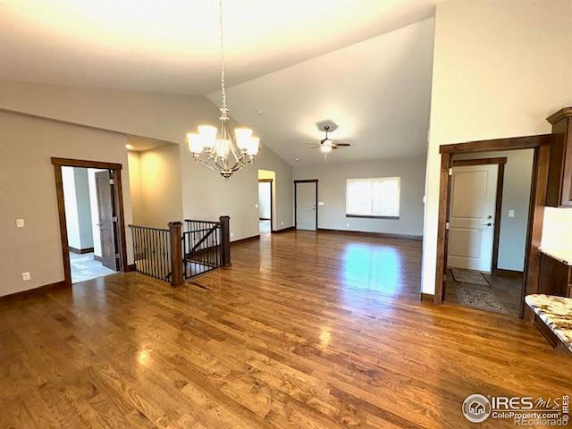 empty room with baseboards, high vaulted ceiling, wood finished floors, and ceiling fan with notable chandelier