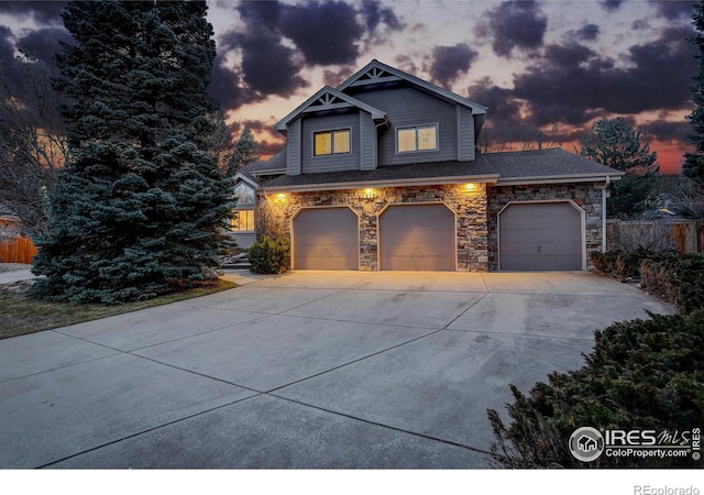 view of front of house featuring stone siding, concrete driveway, and fence