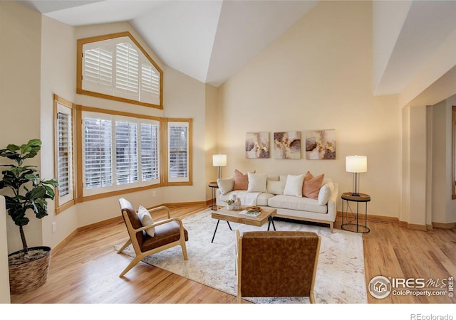 living area featuring high vaulted ceiling, baseboards, and wood finished floors