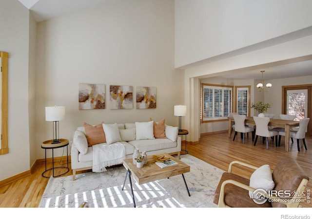 living area with an inviting chandelier, a high ceiling, baseboards, and wood finished floors