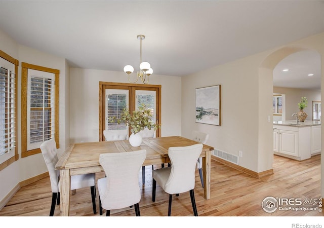 dining space with arched walkways, light wood-type flooring, visible vents, and baseboards