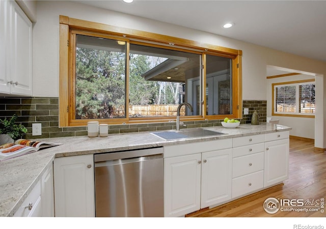 kitchen featuring light wood finished floors, backsplash, white cabinetry, a sink, and dishwasher