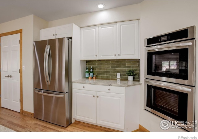 kitchen featuring appliances with stainless steel finishes, white cabinets, light wood-style floors, and decorative backsplash