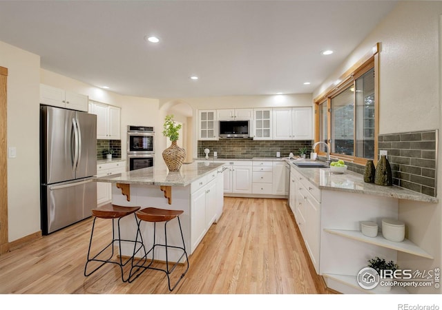 kitchen with stainless steel appliances, a kitchen island, a sink, open shelves, and a kitchen bar