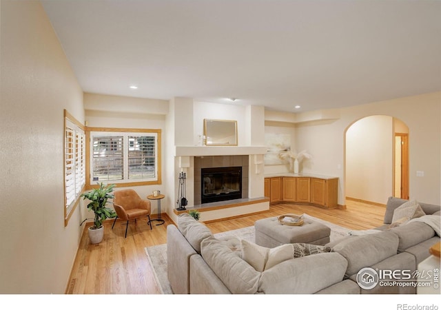 living room with arched walkways, recessed lighting, a tiled fireplace, and light wood-style floors