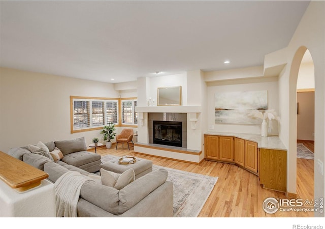 living area featuring arched walkways, light wood finished floors, a fireplace, and recessed lighting