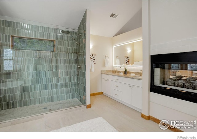 full bath with vaulted ceiling, a tile shower, a sink, and a multi sided fireplace