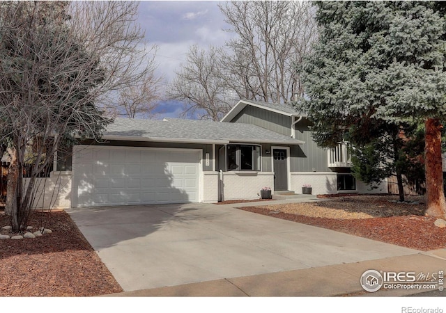 tri-level home with a garage, driveway, brick siding, and a shingled roof