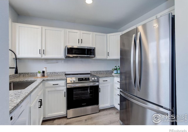 kitchen featuring white cabinets, light wood-style flooring, light stone countertops, stainless steel appliances, and backsplash