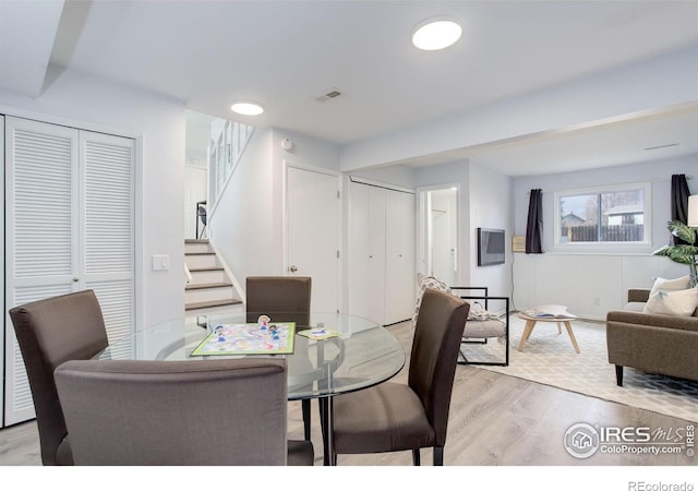 dining room featuring light wood-style flooring, stairs, and visible vents