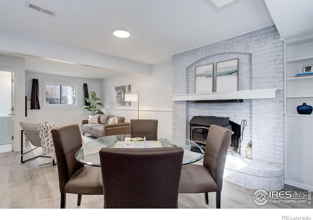 dining room with a wainscoted wall, a fireplace, wood finished floors, and visible vents