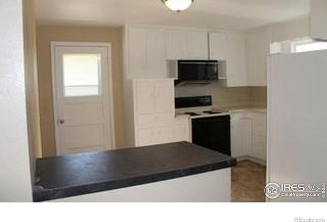 kitchen featuring dark countertops, range with electric cooktop, black microwave, freestanding refrigerator, and white cabinetry