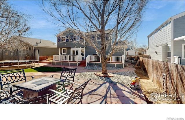 rear view of property with a patio, an outdoor fire pit, a wooden deck, a fenced backyard, and a trampoline