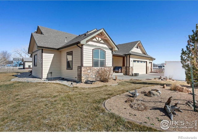 view of front of property featuring a garage, a shingled roof, concrete driveway, stone siding, and a front yard