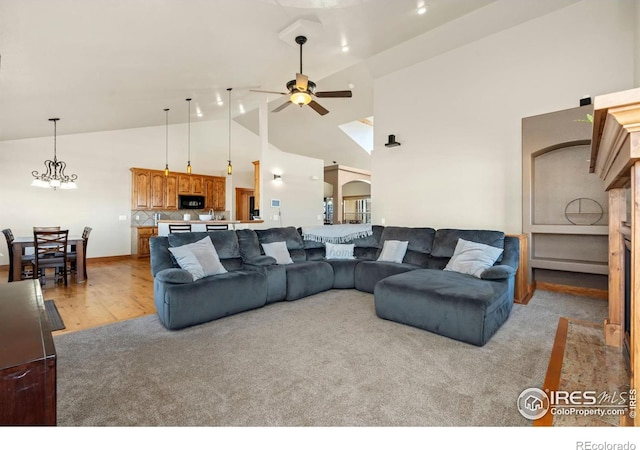 living room with ceiling fan with notable chandelier, high vaulted ceiling, and light wood-style floors