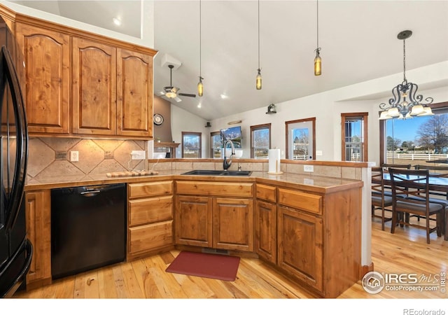 kitchen with plenty of natural light, brown cabinetry, a peninsula, black appliances, and a sink