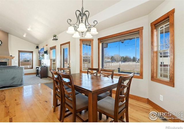 dining area with a notable chandelier, a fireplace, light wood-style flooring, vaulted ceiling, and baseboards