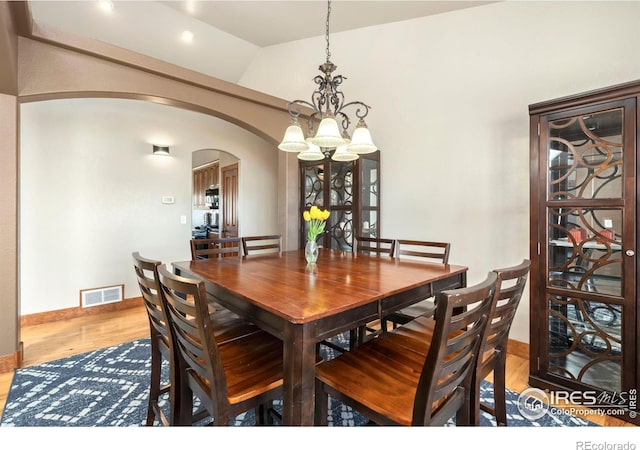 dining space featuring arched walkways, lofted ceiling, wood finished floors, visible vents, and an inviting chandelier