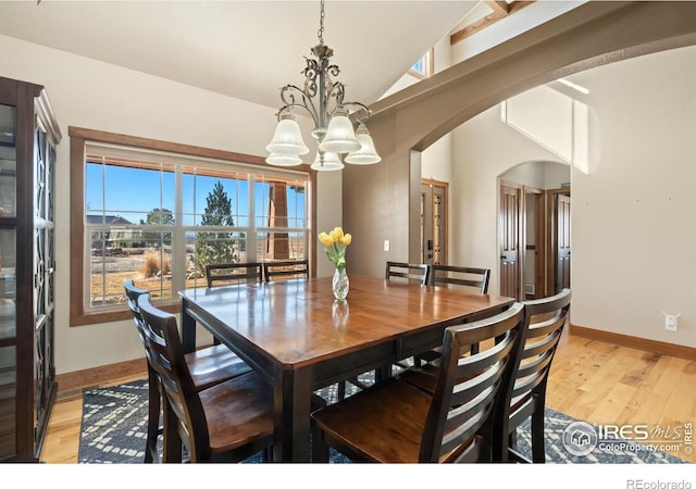 dining area featuring arched walkways, a chandelier, lofted ceiling, baseboards, and light wood finished floors