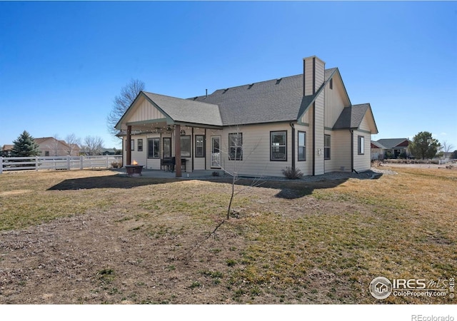 rear view of house with a patio, a chimney, roof with shingles, fence, and a yard